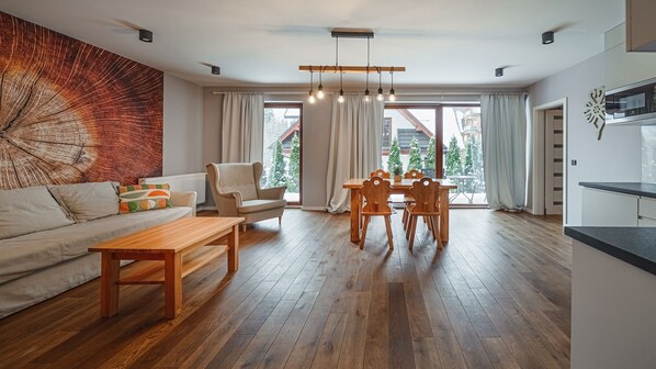 Un salon moderne avec un plancher en bois, un canapé, une table basse, une table à manger avec des chaises et une grande fenêtre avec des rideaux.