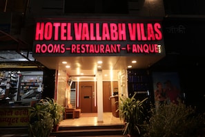 A hotel entrance with a neon sign indicating it offers rooms, a restaurant, and an arcade. - Vallabh Vilas (Narmadapuram)
