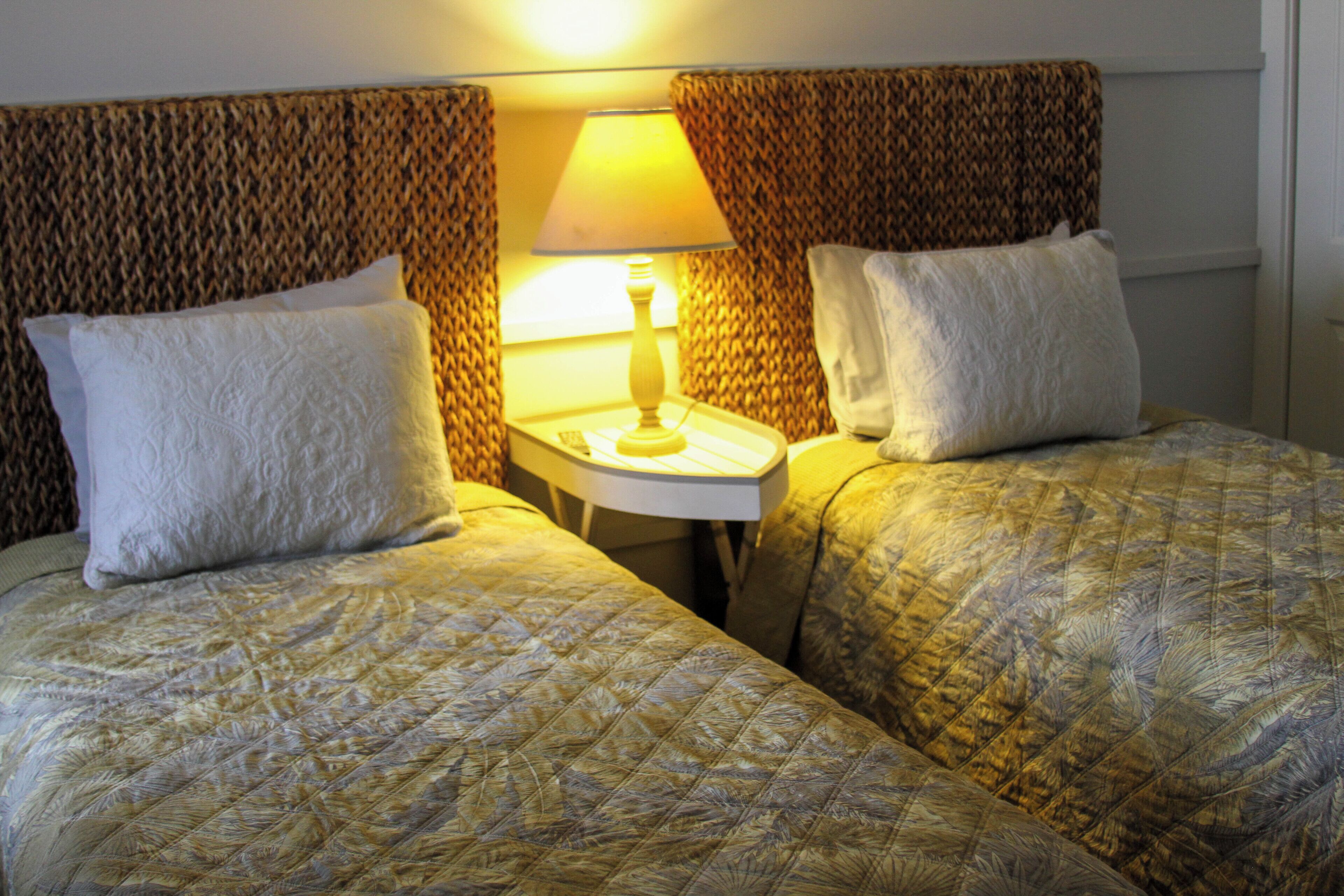 Quarto de hotel com duas camas, uma mesa de cabeceira com abajur e cortinas estampadas.