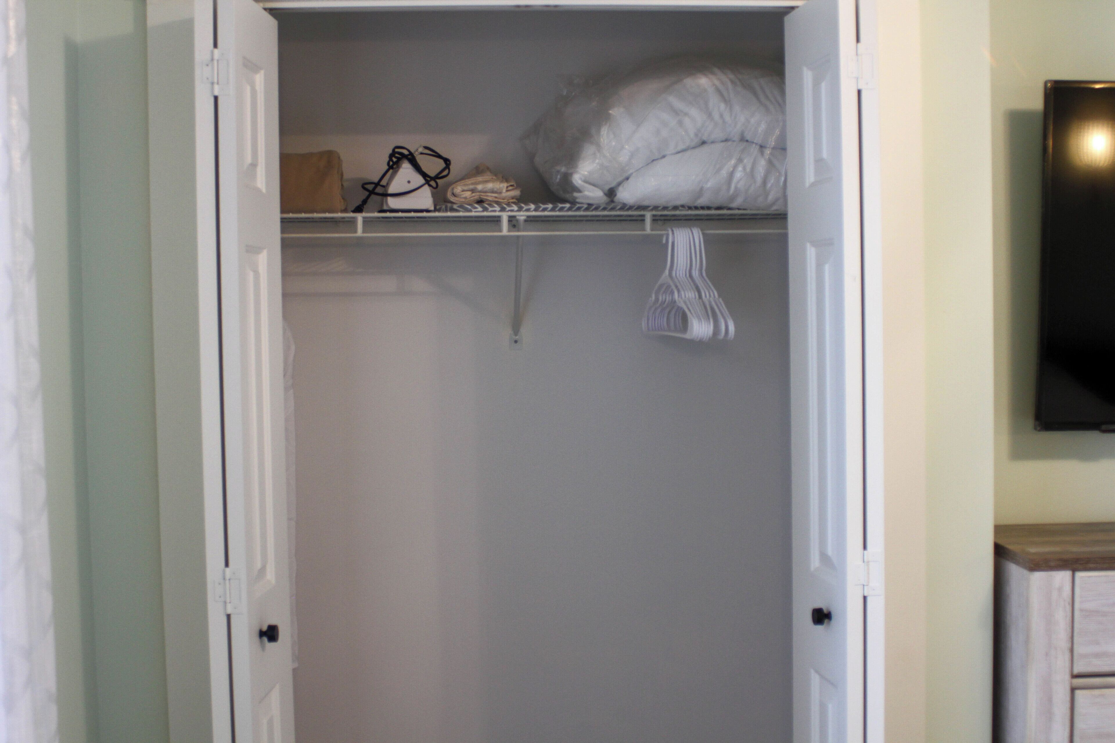 A closet with a hanging rack, a folded blanket, and a pair of shoes.