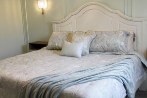 A neatly made bed with a patterned bedspread and pillows, a wooden nightstand, and a wall-mounted light fixture. - Waterway Getaway (Myrtle Beach)