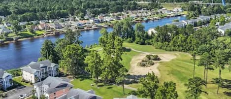 An aerial view of a residential area with a golf course, a body of water, and several buildings.