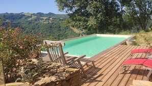 Puinen terassi, jossa on uima-allas, aurinkotuoleja ja näkymä maaseudulle.