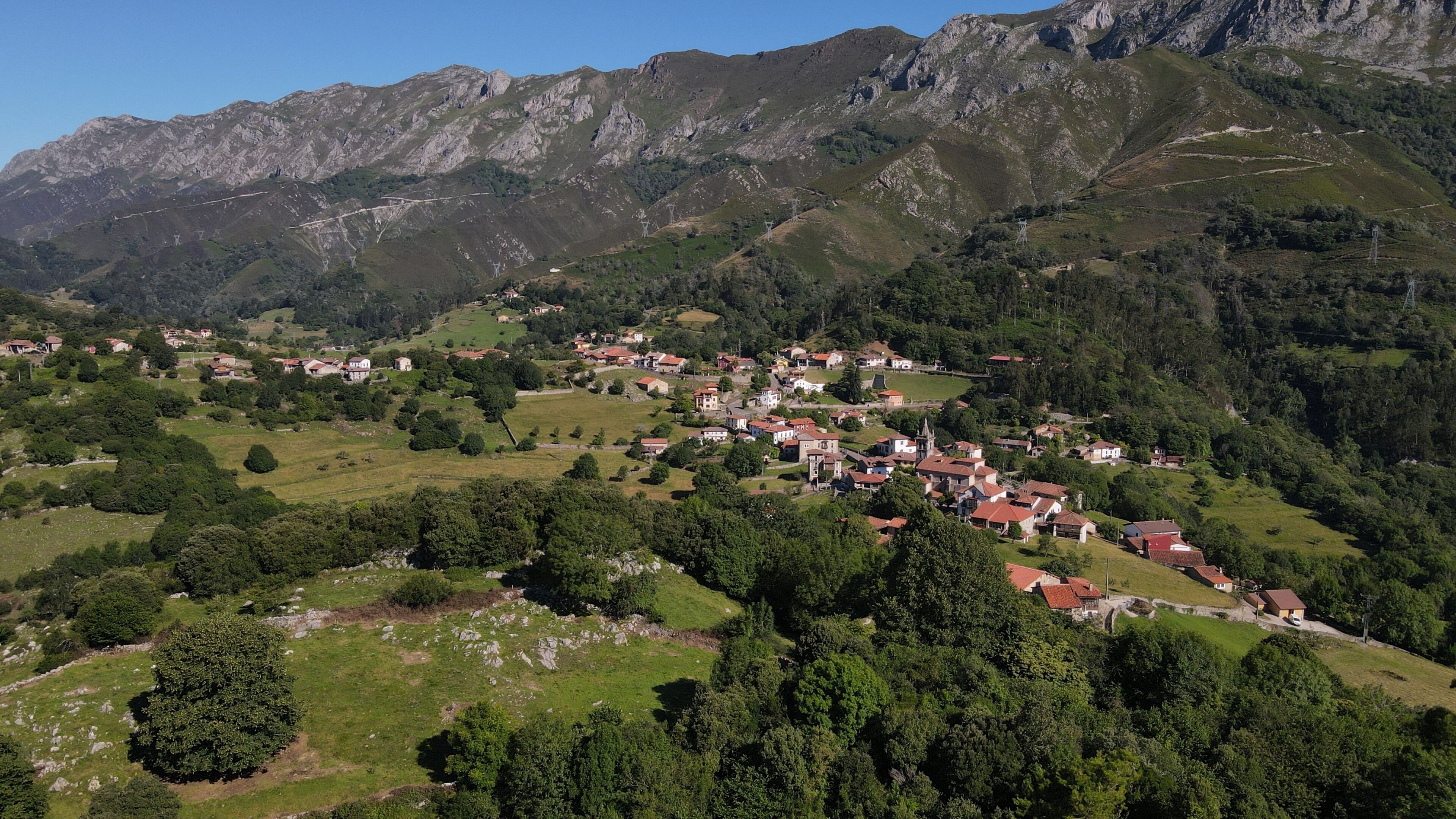 Un village de montagne aux maisons traditionnelles, avec une église et une route sinueuse.