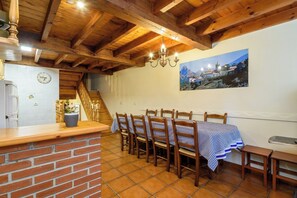 Un espace repas avec des chaises en bois et une nappe à carreaux, un comptoir en briques et un escalier menant à une autre pièce.