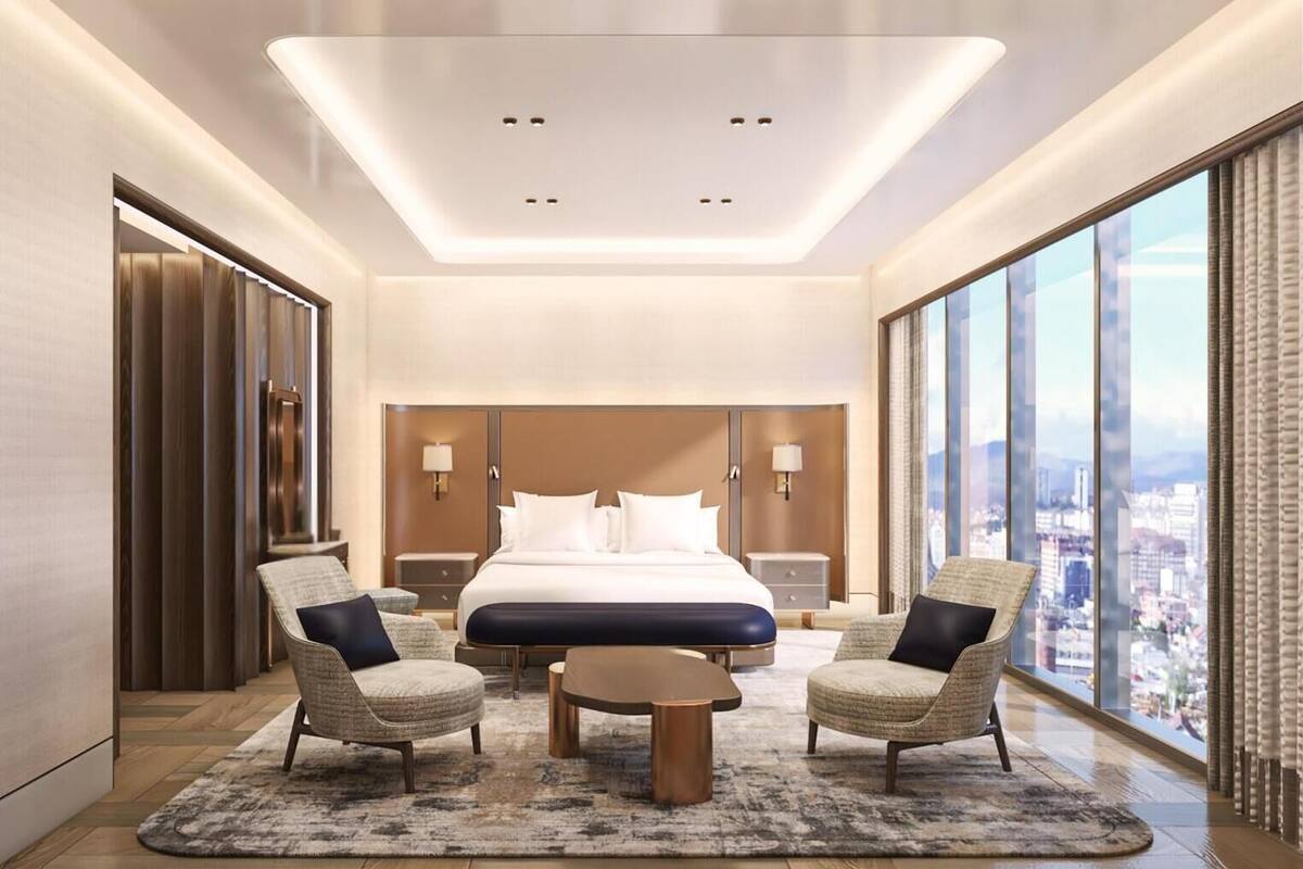 Ein modernes Hotelzimmer mit einem großen Bett, zwei Sesseln, einem Couchtisch und Blick auf die Stadt.