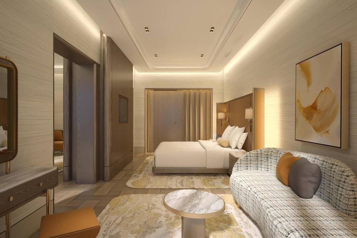 Ein modernes Hotelzimmer mit einem großen Bett, einer Sitzecke mit einer Couch und Sesseln, einem kleinen runden Tisch und einem großen abstrakten Gemälde an der Wand.