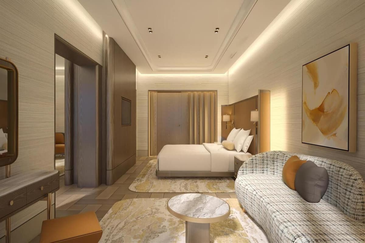 A modern hotel room with a large bed, a sitting area with a sofa and armchairs, a small round table, and a large abstract painting on the wall.