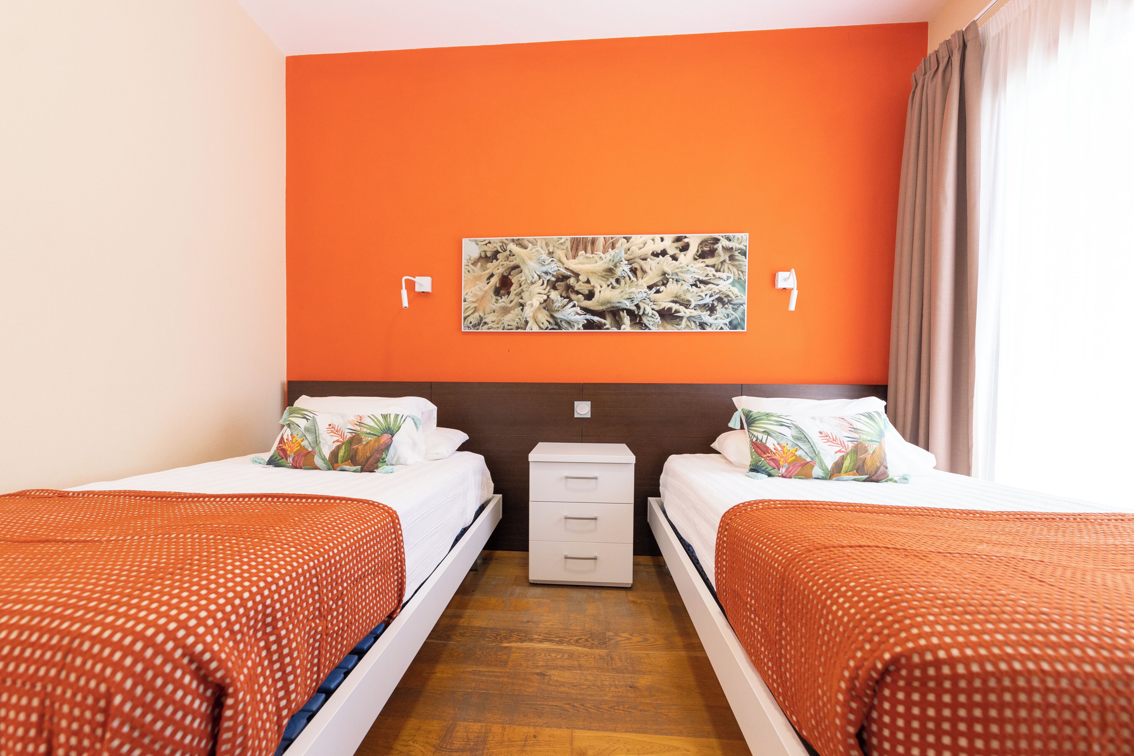 Ein Hotelzimmer mit zwei Betten, einem Nachttisch, einem Wandbild und einem Fenster mit Vorhängen.