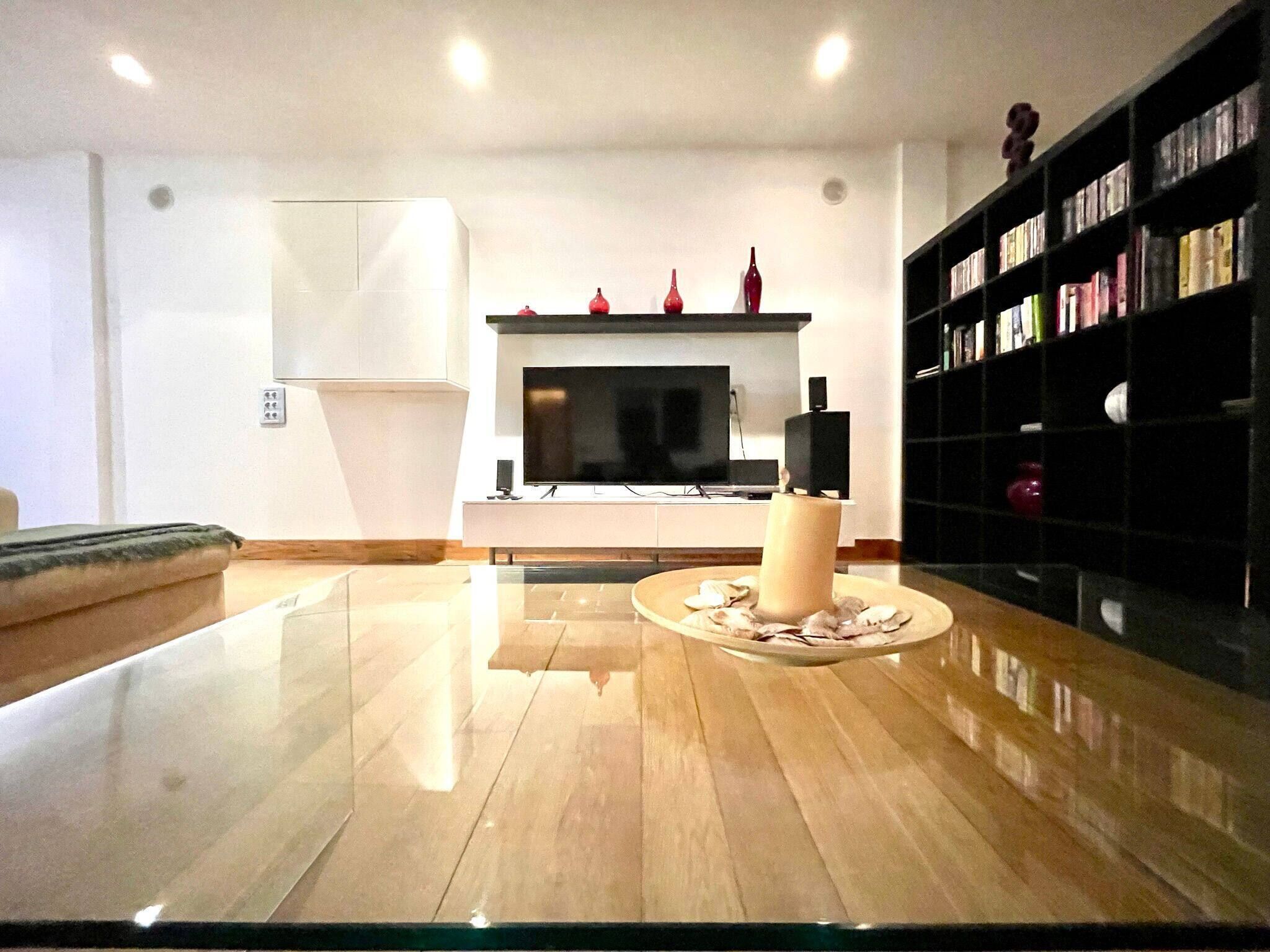 Una sala de estar moderna con una mesa de centro de vidrio, una chimenea con jarrones rojos, una estantería y un televisor de pantalla plana.
