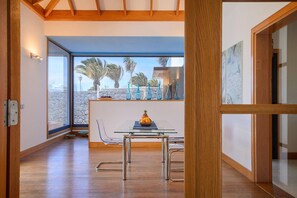 A modern kitchen with a glass dining table, a bowl of fruit, and a view of palm trees through large windows. - Playas Blanca Pool Private Villas (Playa Blanca)