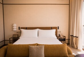 Una habitación de hotel con cama, mesitas de noche, lámpara, radio y ventana con cortinas.