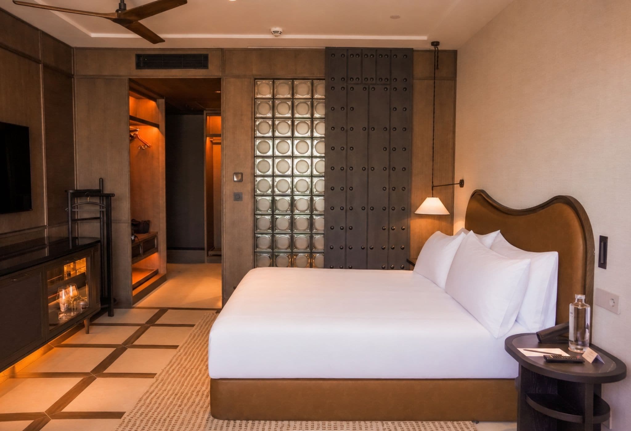 Quarto de hotel com uma cama grande, televisão, minibar e uma parede com desenhos circulares.