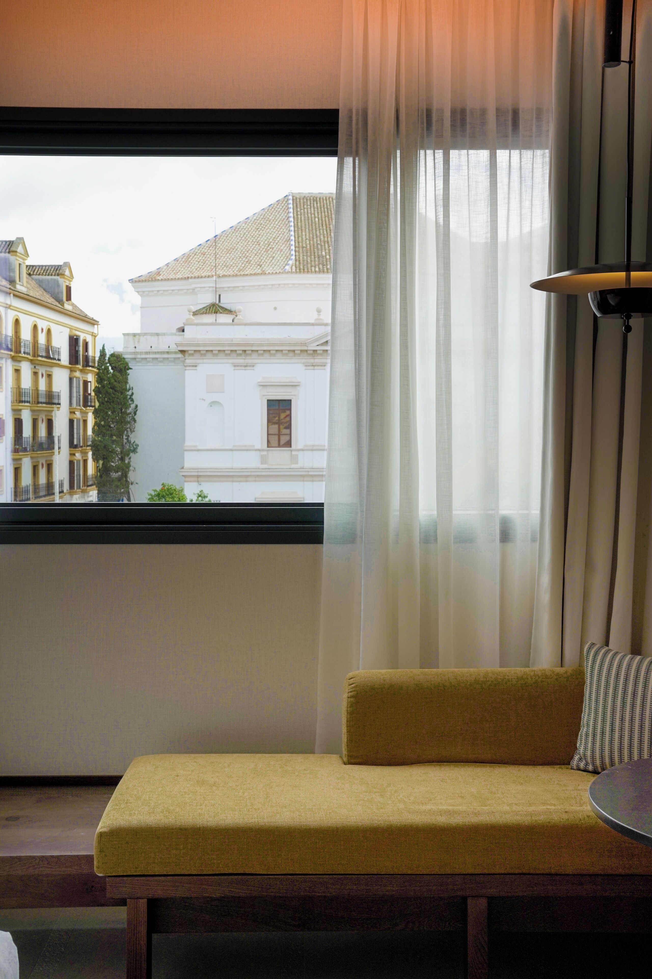 A room with a sofa, a table, and a window with sheer curtains.
