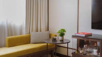 A room with a sofa, a small round table with a plant and a book, a cabinet with bottles, and a TV on the wall.