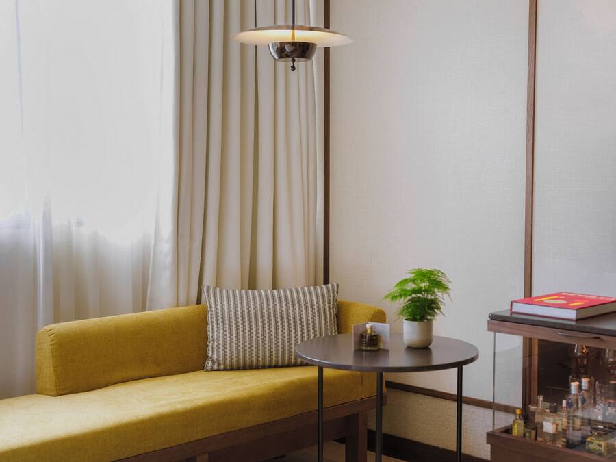 A room with a sofa, a small round table with a plant and a book, a cabinet with bottles, and a TV on the wall.