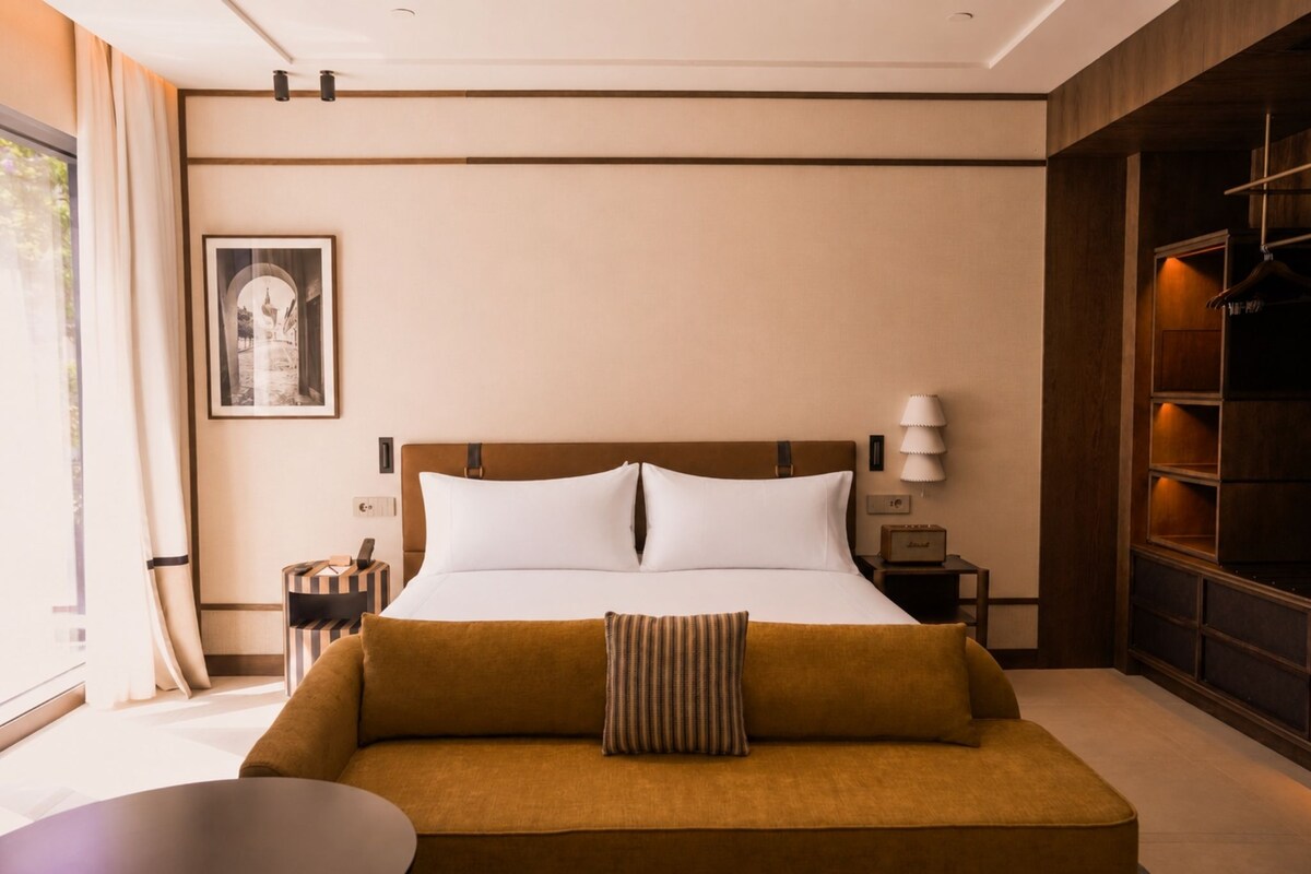 A hotel room with a bed, a sofa, a bedside table, a lamp, a picture on the wall, and a window with curtains.