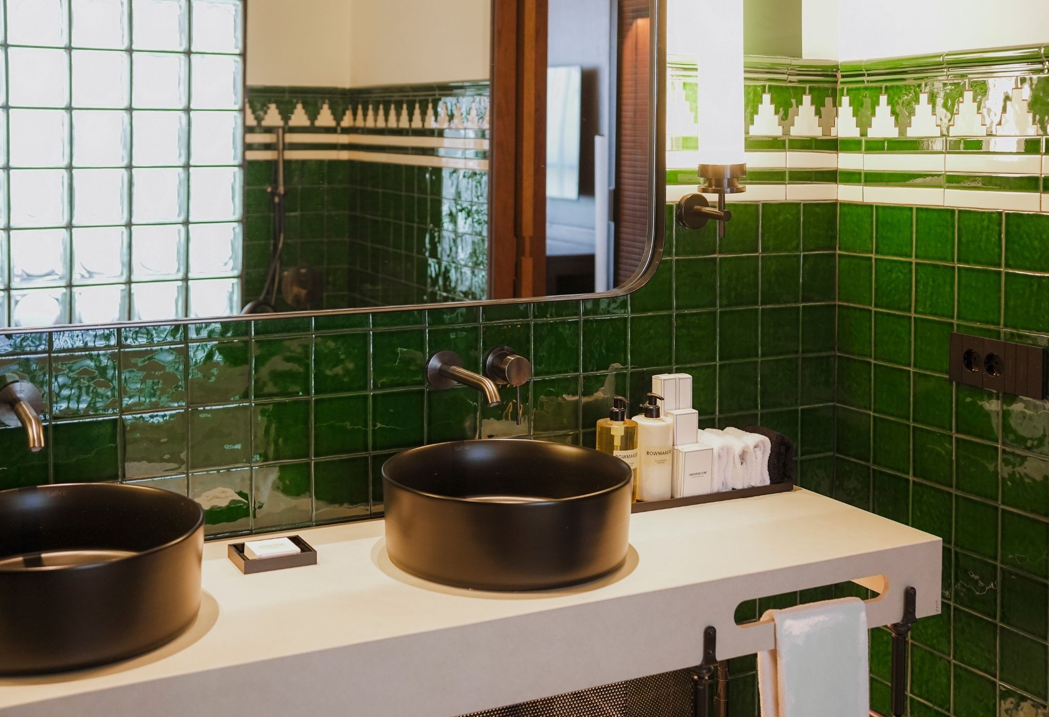 A bathroom with two sinks, a mirror, and green tiled walls.