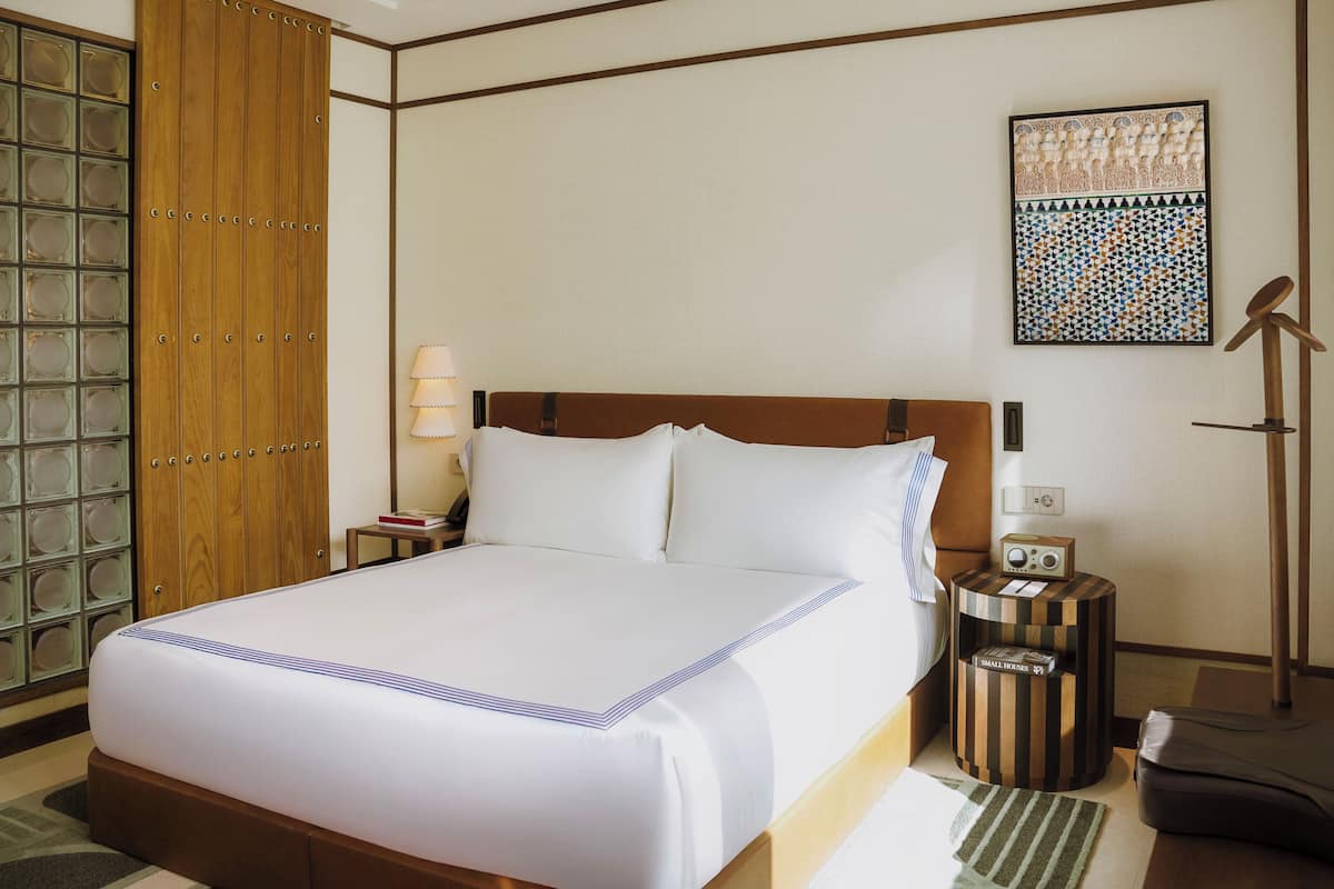 A hotel room with a large bed, a wooden wardrobe, a bedside table with a lamp, and a radio.