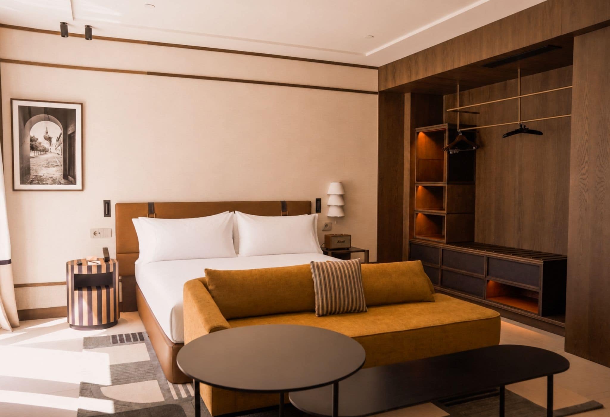 Ein Hotelzimmer mit einem Bett, einem Schlafsofa, einem kleinen Tisch, einem Mülleimer, einer Lampe, einem Kleiderhaken und einem gerahmten Bild an der Wand.