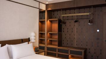 A hotel room with a bed, a bedside table, a lamp, a wardrobe with shelves, and a coat rack.