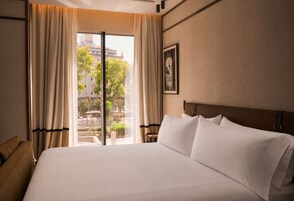 A hotel room with a large bed, a view of the outdoors, and a framed picture on the wall.