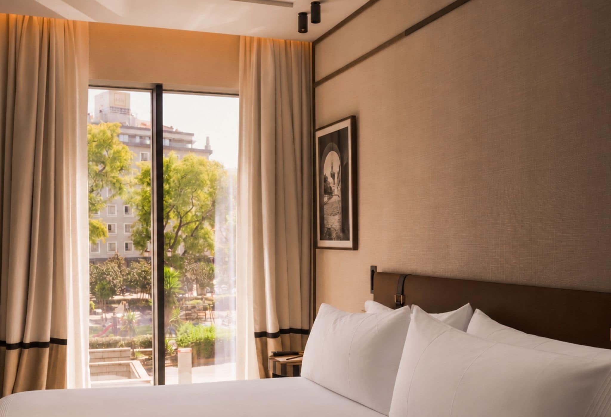 Camera d'albergo con un letto grande, vista sullo skyline urbano tramite una porta scorrevole e un quadro appeso al muro.