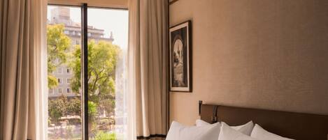 Camera d'albergo con un letto grande, vista sullo skyline urbano tramite una porta scorrevole e un quadro appeso al muro.