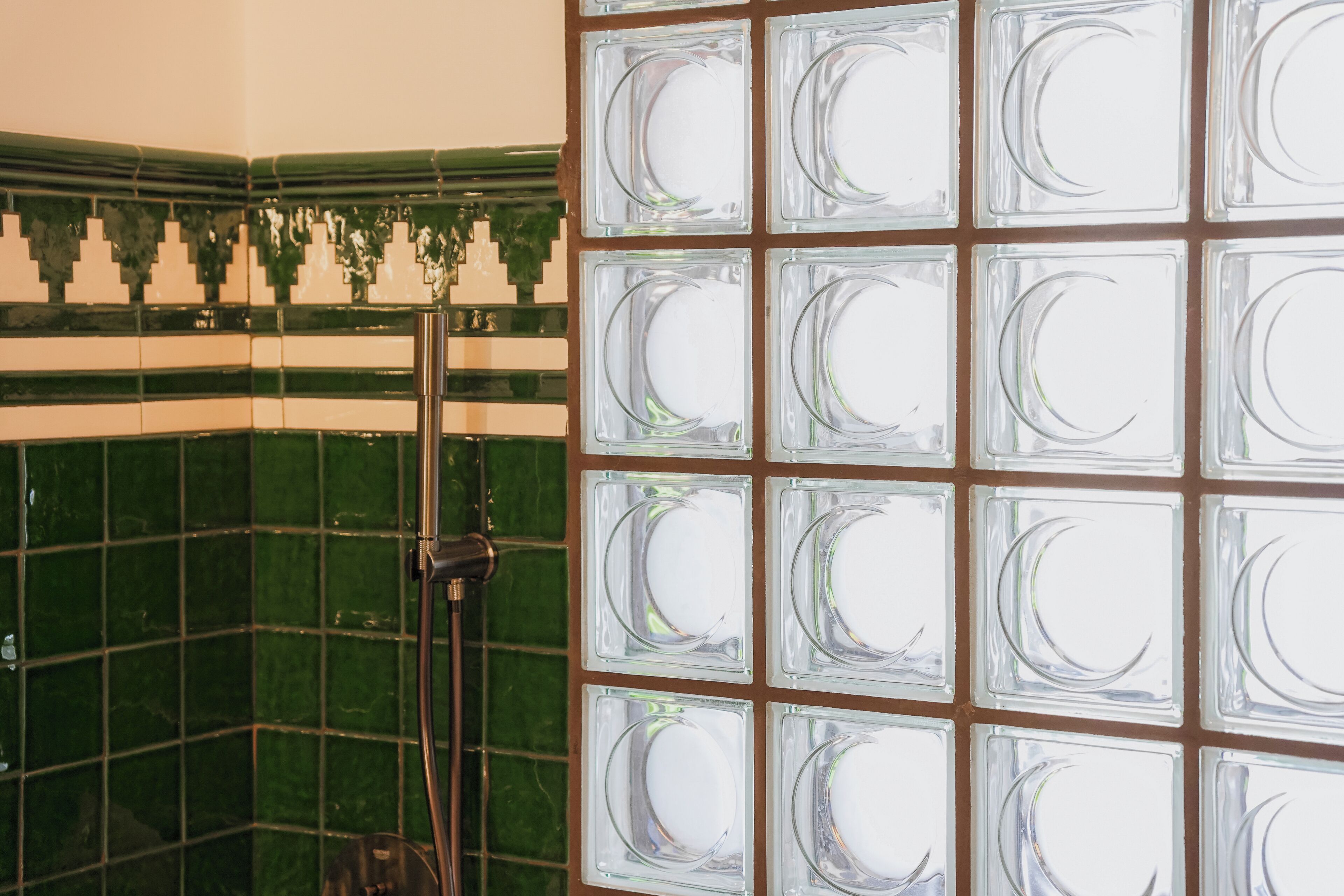 Un baño con paredes de azulejos verdes, zona de ducha y mampara de cristal con diseño de luna creciente.