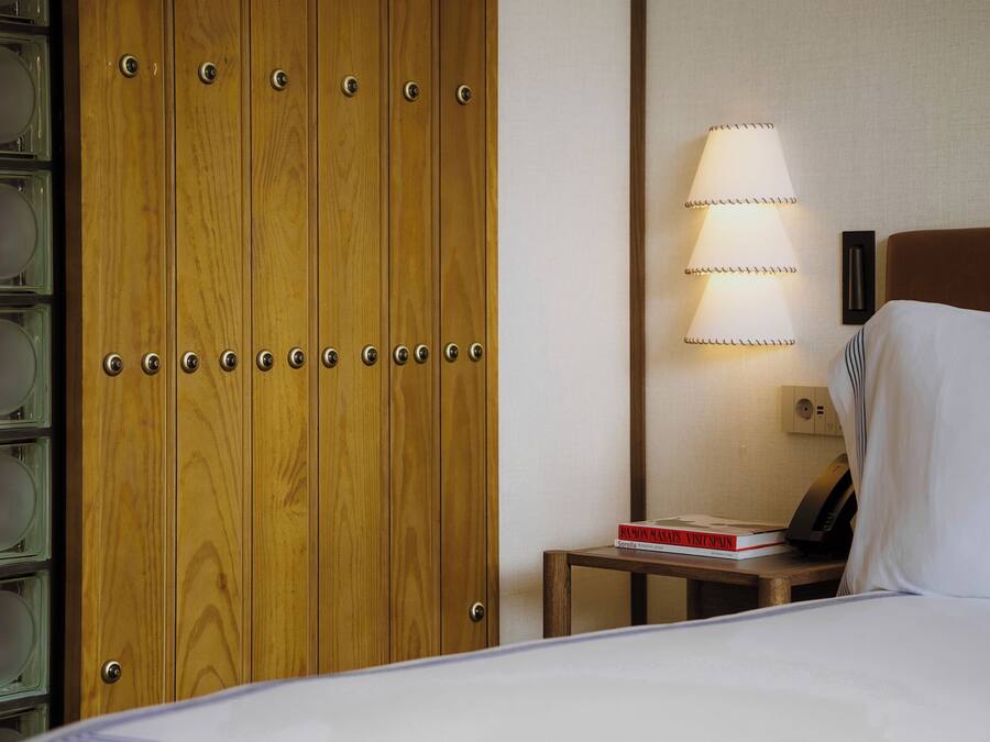 Habitación de hotel con un armario de madera, una mesita de noche con lámpara y una cama con almohada.