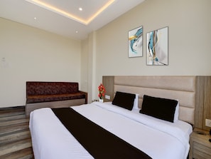 Une chambre d’hôtel avec un grand lit, une tête de lit en bois, un canapé rouge et des œuvres d’art abstraites accrochées au mur.