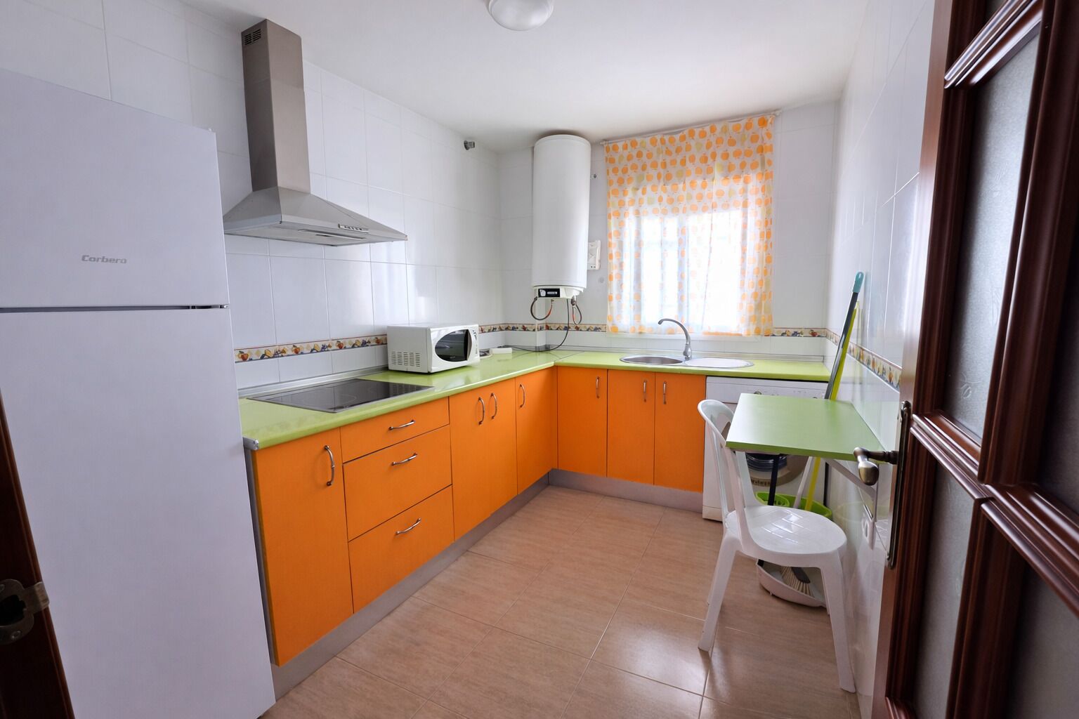 A compact kitchen with white and orange cabinets, a white refrigerator, a microwave, and a sink.