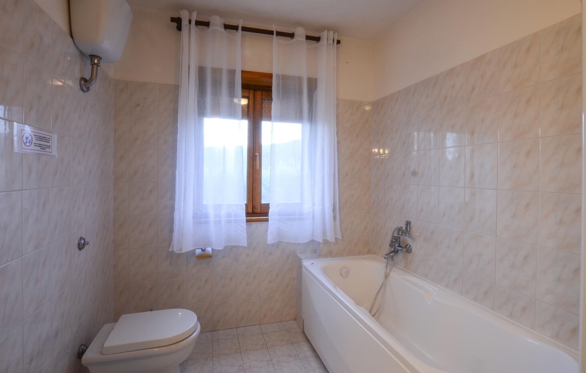 A bathroom with a toilet, a bathtub, and a window with sheer curtains.