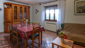 A dining area with a wooden cabinet, a dining table with chairs, a radiator, a window with curtains, and a painting on the wall. - Lovely home in Santa Fiora (Santa Fiora)