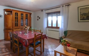 A dining area with a wooden cabinet, a dining table with chairs, a radiator, a window with curtains, and a painting on the wall. - Lovely home in Santa Fiora (Santa Fiora)