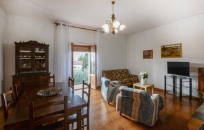 Ein Wohnzimmer mit Esstisch, Stühlen, einer Couch, einem Fernseher und einer Deckenleuchte.