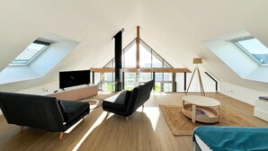 A spacious loft bedroom with a large skylight, a modern black sofa, a small round table, and a bed with a blue blanket. - Architect-designed villa with sea view (Le Conquet)