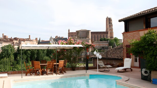 Une piscine avec des chaises longues, une table et une pergola ornée de fleurs.