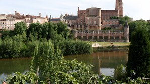 Un bâtiment historique doté d’une tour imposante, entouré d’une végétation luxuriante et bordé par une rivière paisible.
