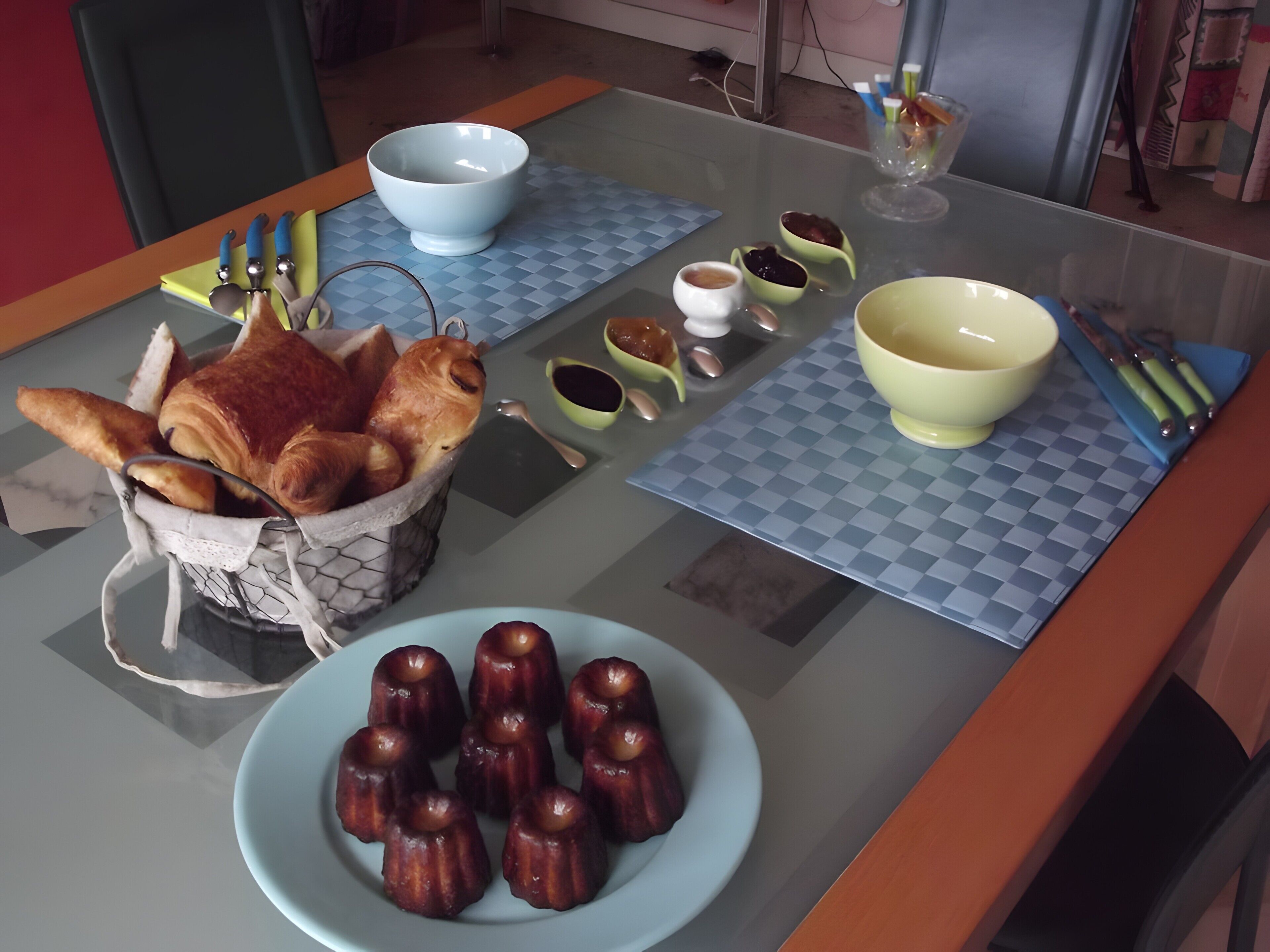 Een tafel met een mand croissants, een bord kleine gebakjes, en diverse kommen en bestek.