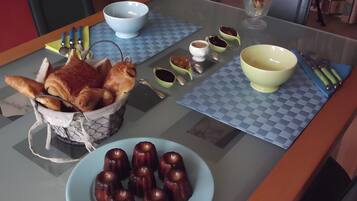 Een tafel met een mand croissants, een bord kleine gebakjes, en diverse kommen en bestek.