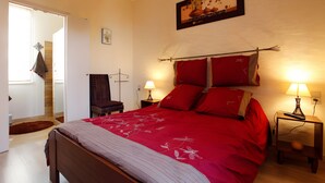 Une chambre à coucher avec un lit, deux tables de chevet avec des lampes, une chaise, une porte et un tableau accroché au mur.