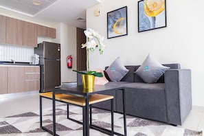 Ein modernes Wohnzimmer mit einem grauen Sofa, einem kleinen Tisch und einer Küchenzeile im Hintergrund.