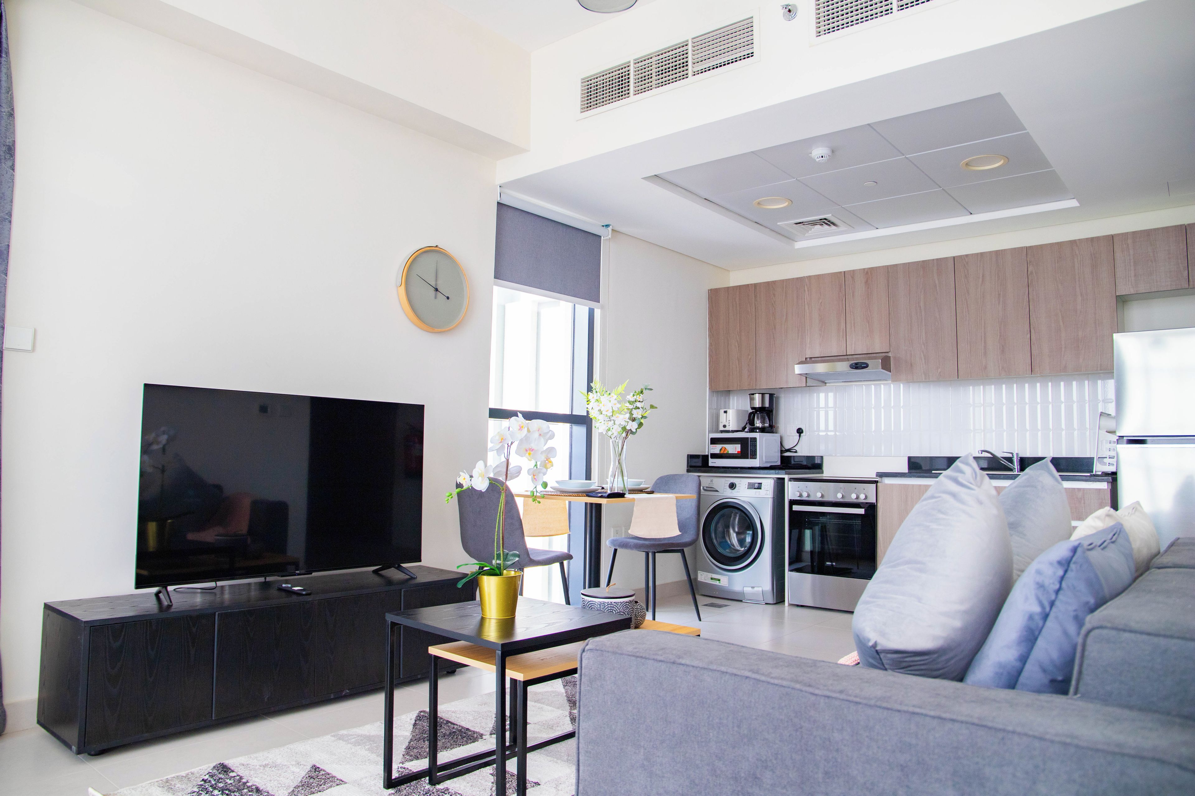 A modern living room with a flat-screen TV, a sofa, a coffee table, and a dining area with a table and chairs.