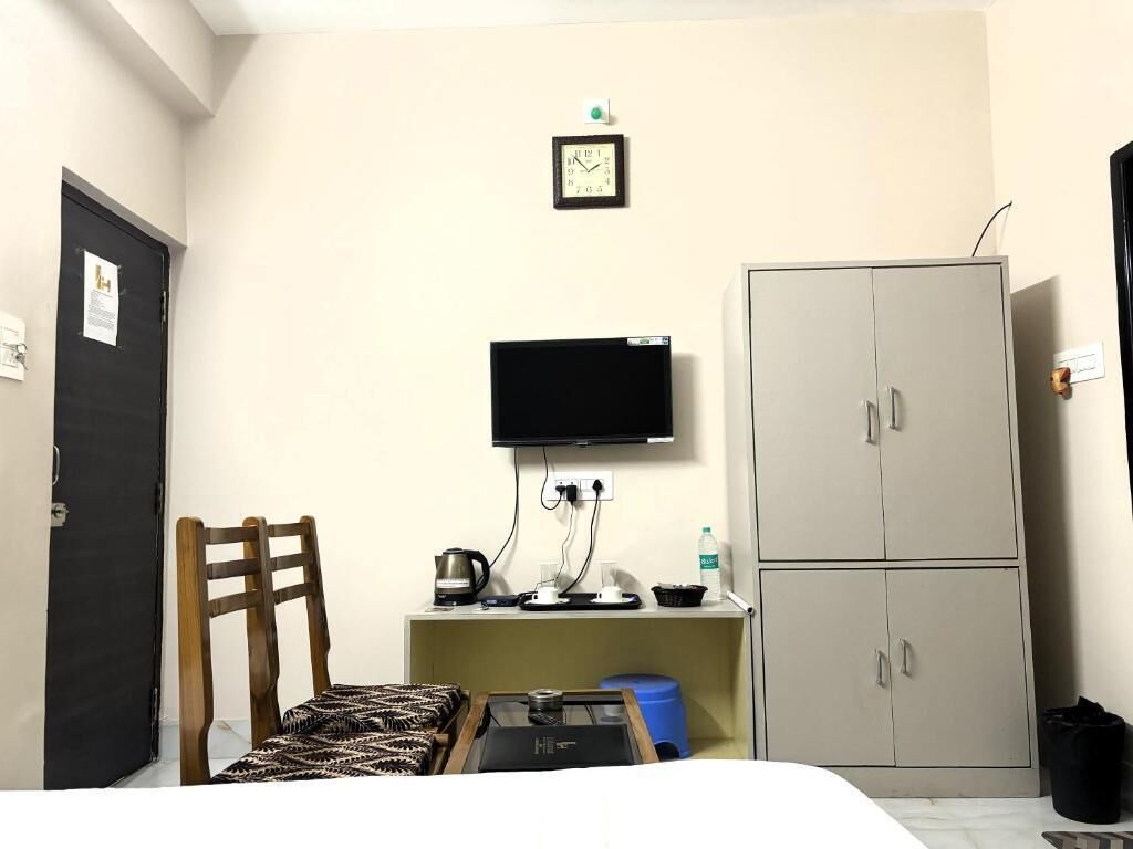 A hotel room with a bed, a desk with a computer, a television, a wardrobe, and a door.