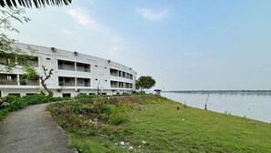 Un bâtiment moderne à plusieurs étages, doté d’une allée pavée et d’une zone herbeuse située à côté d’une étendue d’eau calme.