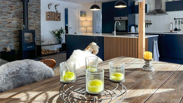 A modern kitchen with dark cabinetry, a central island, and a dining area with a wooden table and candles. - 3 bedroom awesome home in Farsø (Farsø)