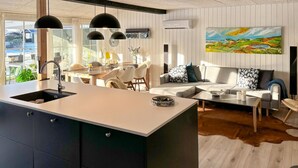 A modern kitchen with a central island, dining area with chairs, a sofa, and a painting on the wall. - 3 bedroom awesome home in Farsø (Farsø)