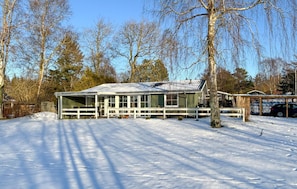 Una casa moderna con un amplio ventanal, rodeada de nieve y árboles.