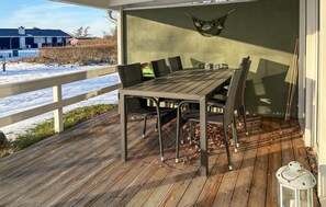 A covered outdoor dining area with a wooden table and chairs, a hammock, and a lantern.